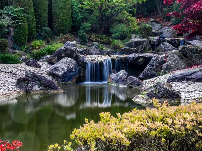Lago ornamental com cascata entre pedras e jardim