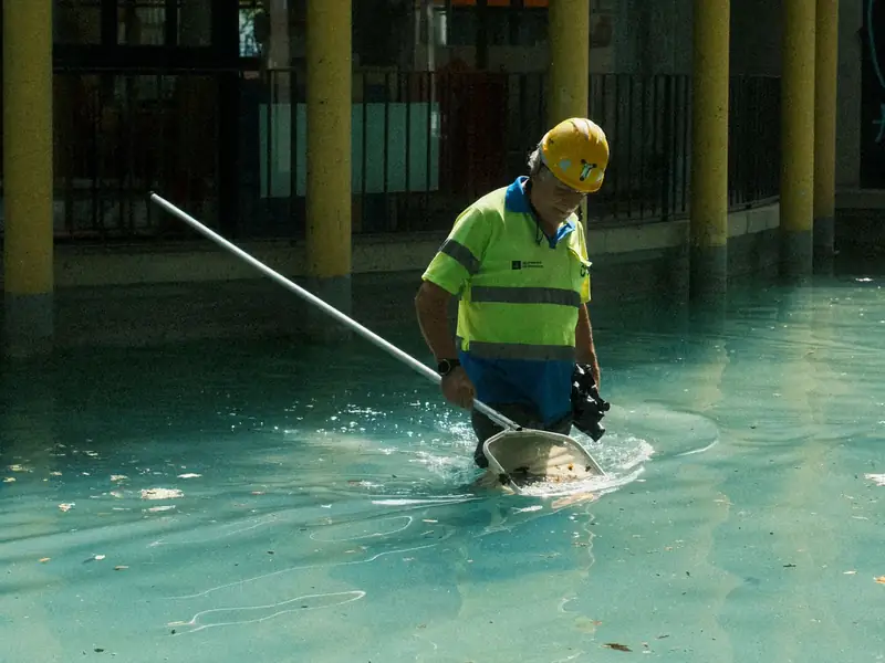 Técnico de manutenção limpando piscina com peneira de cabo longo